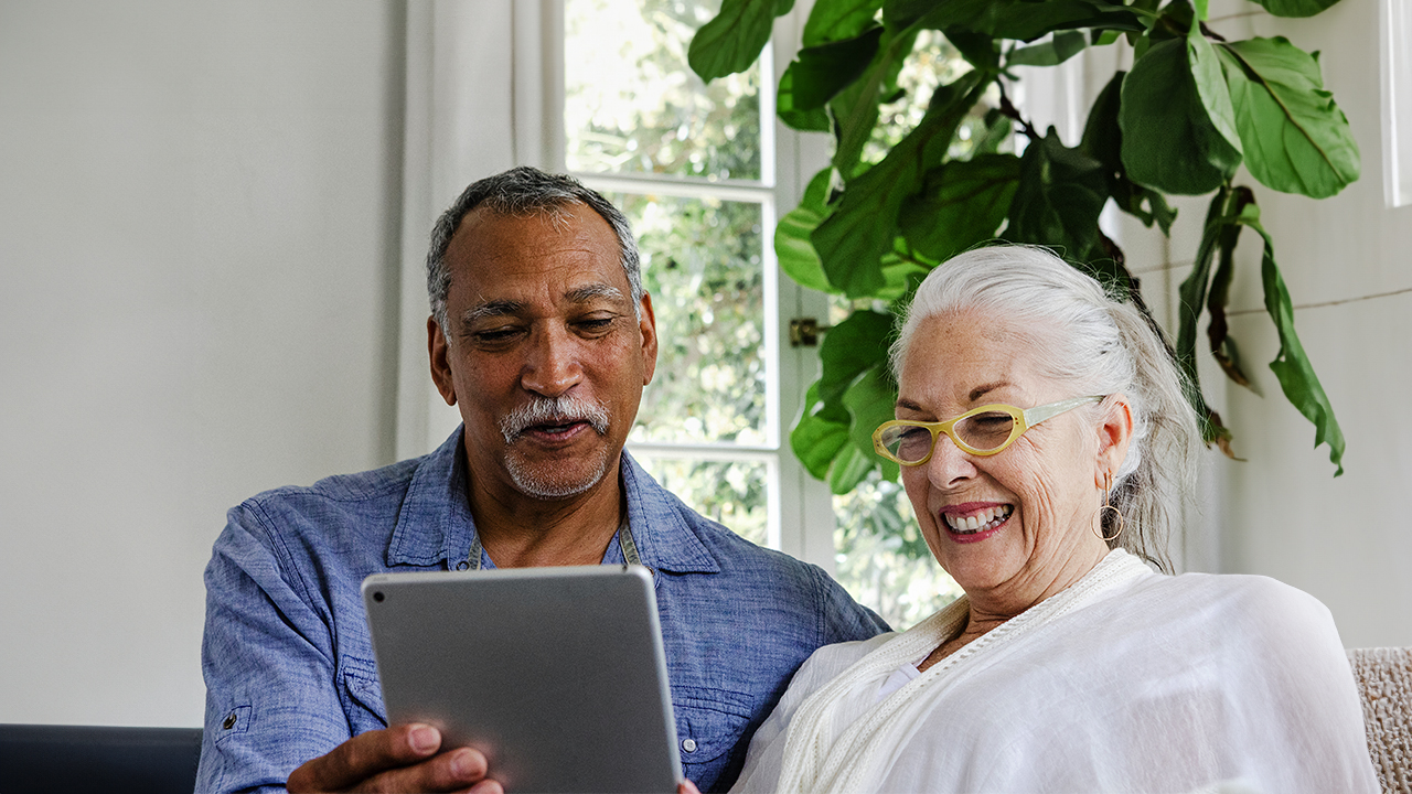 An older couple laughing while viewing a tablet