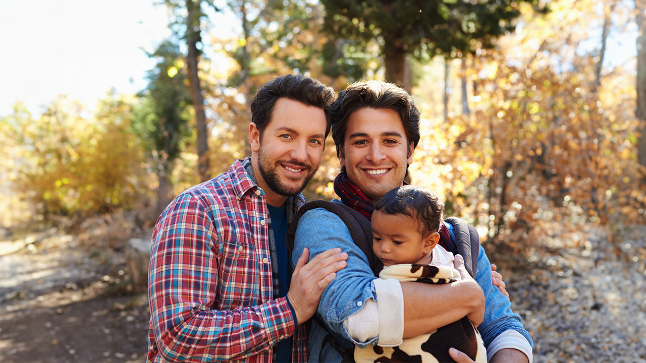 A gay couple poses for a pic with their baby